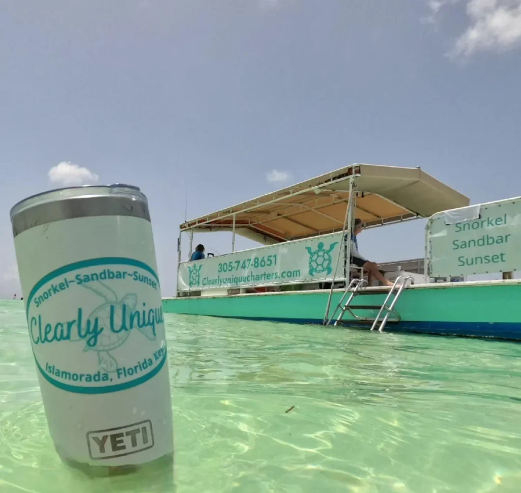 A smiling guest in a tropical sun hat enjoying a beverage while another relaxes on a floating tube in the clear Islamorada water.