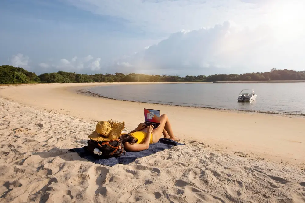 Long shot woman working at beach with laptop.