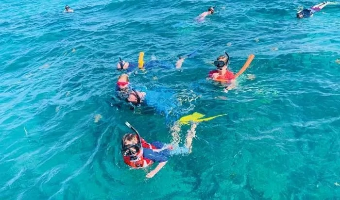 A group of people wearing masks and snorkels swim together in clear, bright blue ocean water.