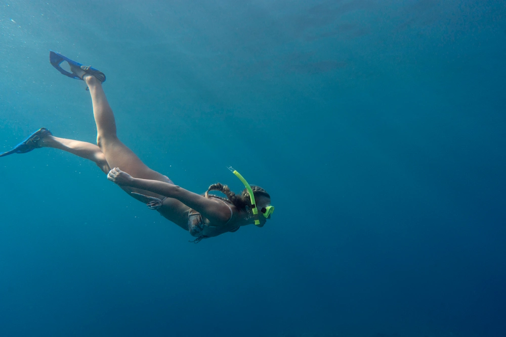 Snorkeler swimming in tropical blue water near coral reef formations