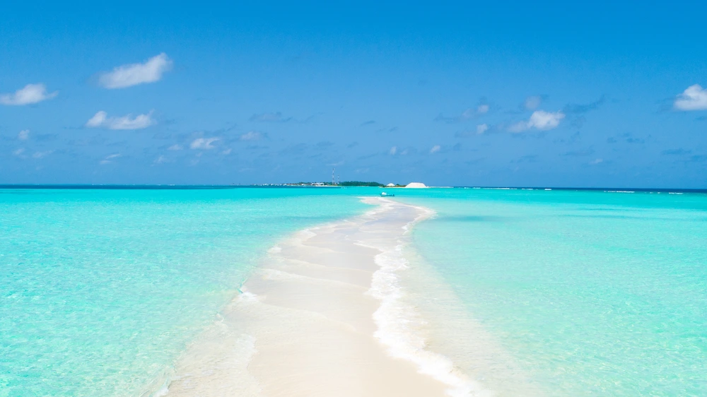 Shallow ocean sandbar surrounded by clear turquoise water and blue sky