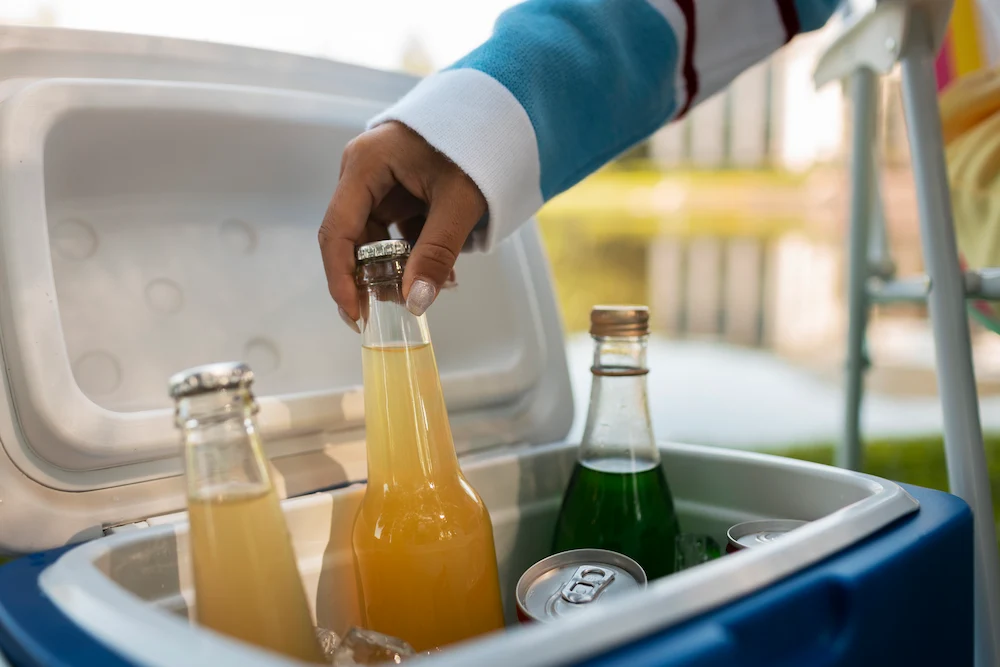 Hand placing a bottled drink into a cooler filled with beverages and ice